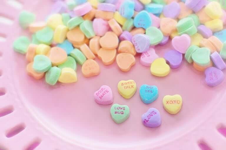 Vibrant pastel heart-shaped Valentine's Day candies on a pink plate with romantic messages.